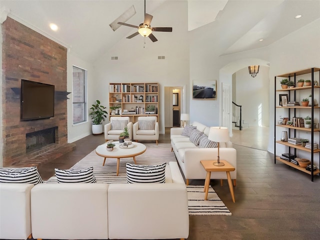 living area featuring arched walkways, high vaulted ceiling, a fireplace, wood finished floors, and a ceiling fan