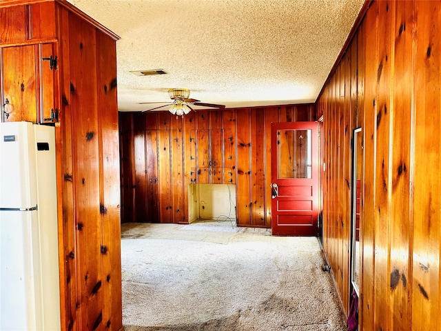 unfurnished room with wood walls, a textured ceiling, visible vents, and carpet flooring