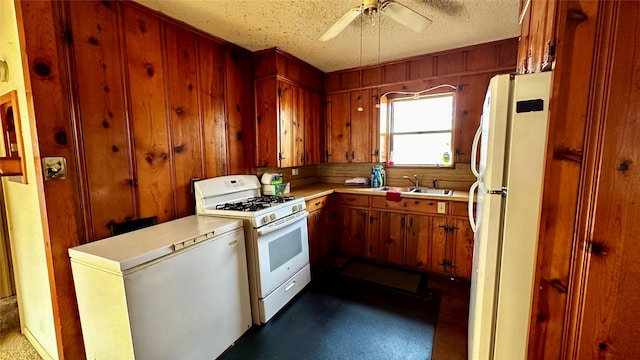 kitchen featuring white appliances, wooden walls, light countertops, a textured ceiling, and a sink