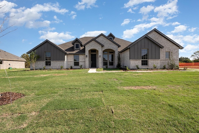 french provincial home featuring board and batten siding, brick siding, and a front lawn