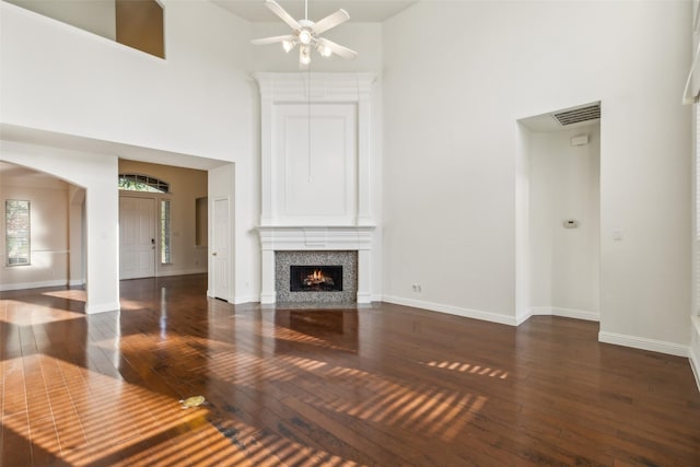 unfurnished living room with a towering ceiling, hardwood / wood-style flooring, visible vents, and arched walkways