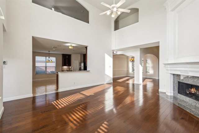 unfurnished living room with arched walkways, hardwood / wood-style flooring, ceiling fan with notable chandelier, a premium fireplace, and baseboards