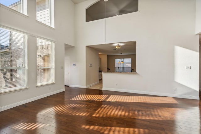 unfurnished living room with a chandelier, wood-type flooring, a high ceiling, and baseboards