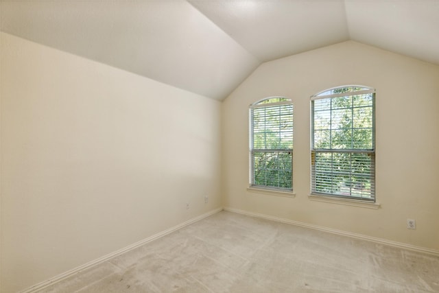 unfurnished room with lofted ceiling, light colored carpet, and baseboards