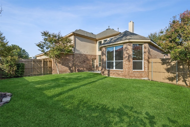 rear view of house featuring a yard, brick siding, a chimney, and a fenced backyard