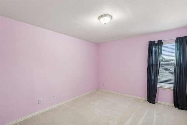 empty room with light carpet, baseboards, and a textured ceiling