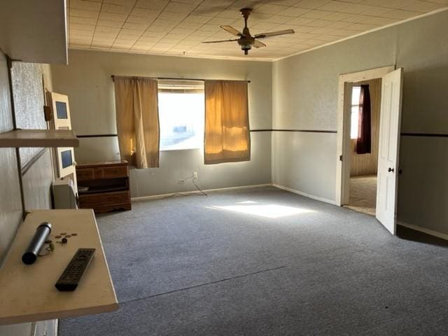 interior space featuring carpet floors, crown molding, baseboards, and a ceiling fan