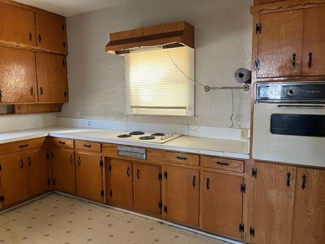 kitchen featuring brown cabinetry, white appliances, light countertops, and light floors