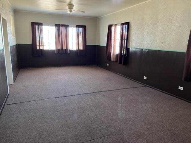 spare room featuring a wainscoted wall, ceiling fan, and crown molding