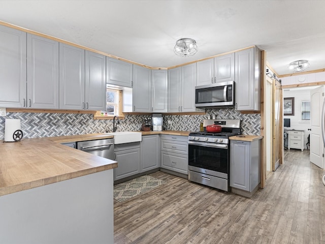 kitchen featuring light wood finished floors, appliances with stainless steel finishes, butcher block counters, and gray cabinetry