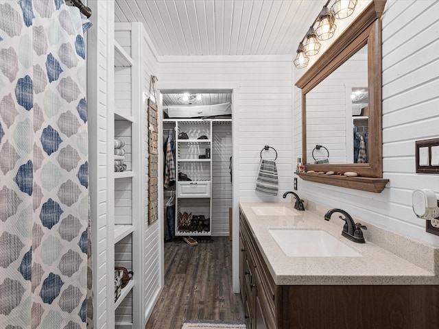 bathroom featuring double vanity, wooden walls, a sink, and wood finished floors