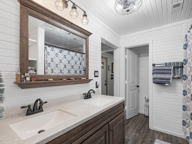 full bathroom with double vanity, a sink, wood walls, and wood finished floors