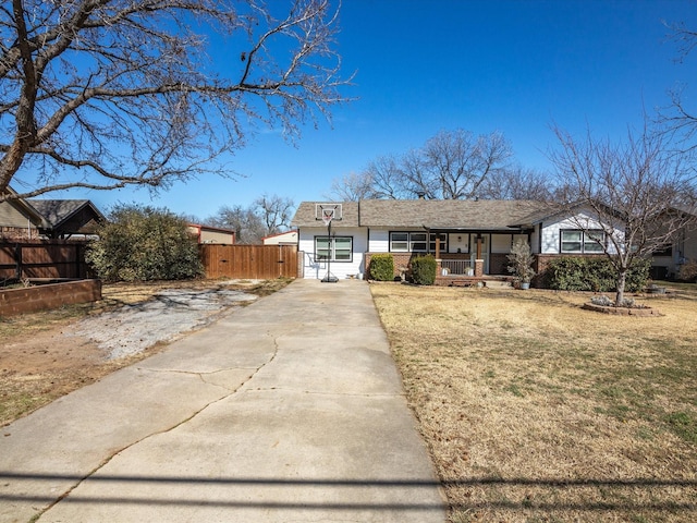 view of front facade with concrete driveway, covered porch, fence, a front yard, and brick siding