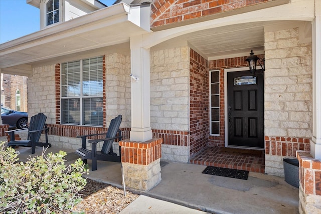 entrance to property featuring a porch and brick siding