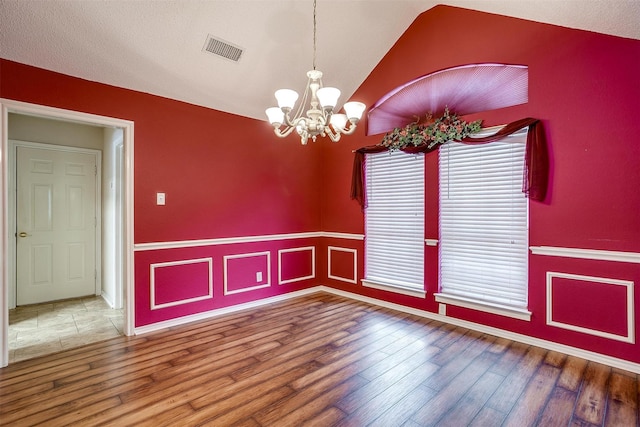 unfurnished dining area featuring vaulted ceiling, a notable chandelier, wood finished floors, and visible vents