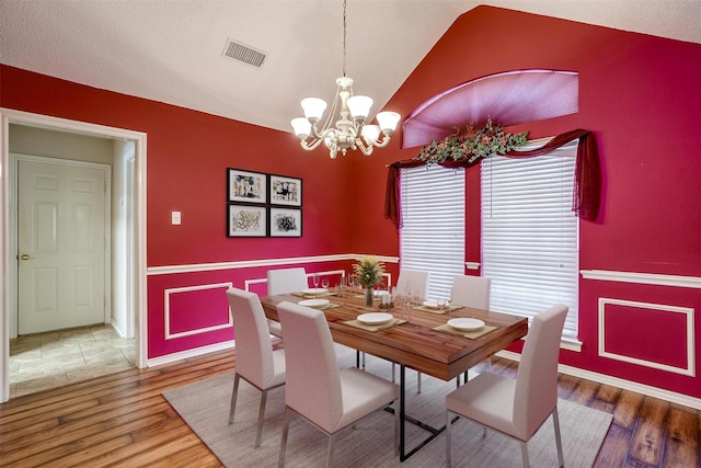 dining space with visible vents, a chandelier, lofted ceiling, wood finished floors, and a textured ceiling