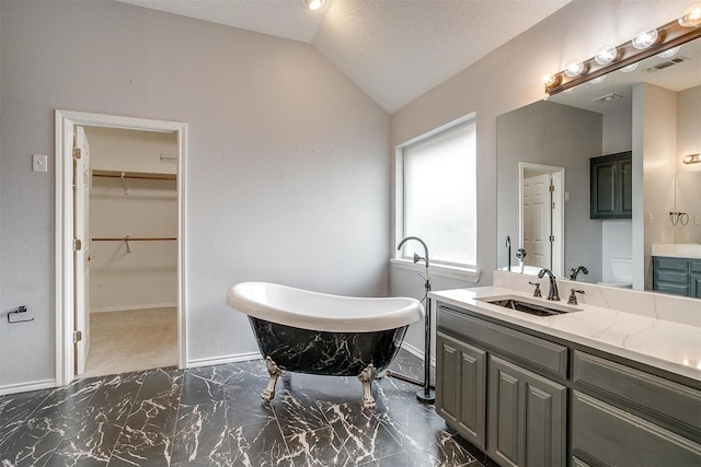 full bath featuring a freestanding tub, marble finish floor, baseboards, vanity, and vaulted ceiling