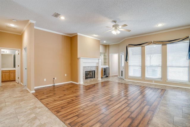 unfurnished living room featuring visible vents, a fireplace, ceiling fan, ornamental molding, and light wood-style floors