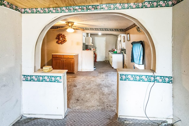 interior space featuring arched walkways, carpet, a ceiling fan, and brown cabinets