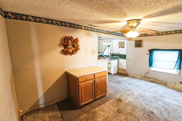 interior space featuring a textured ceiling, ceiling fan, baseboards, dark colored carpet, and brown cabinetry