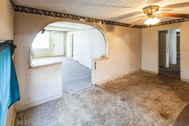 spare room with a textured ceiling, carpet floors, ceiling fan, and arched walkways