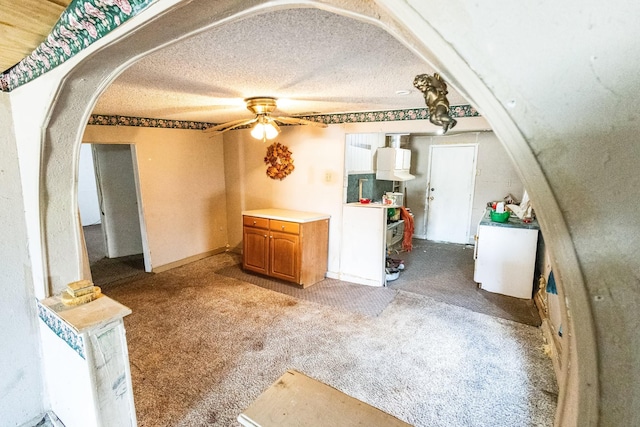 unfurnished living room with ceiling fan, arched walkways, a textured ceiling, and light colored carpet