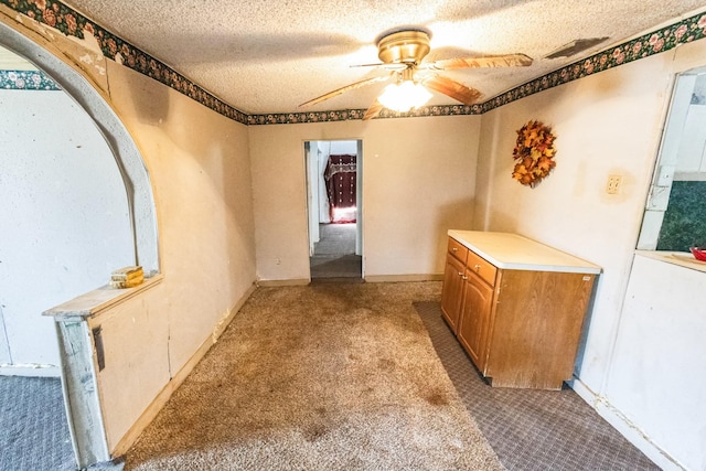 unfurnished dining area with carpet floors, visible vents, a textured ceiling, and a ceiling fan