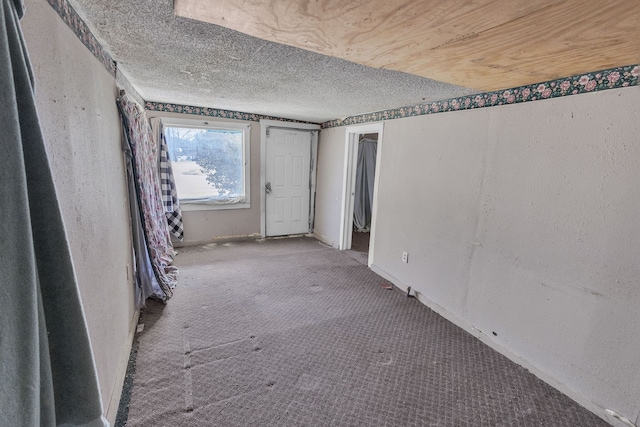 carpeted empty room featuring a textured ceiling and baseboards