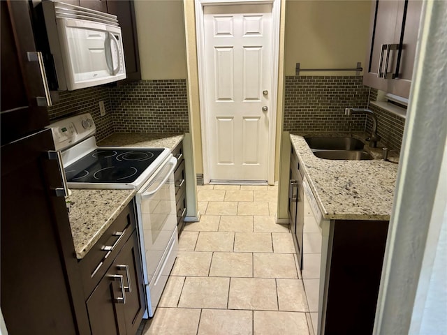 kitchen with light stone counters, light tile patterned floors, a sink, dark brown cabinetry, and white appliances