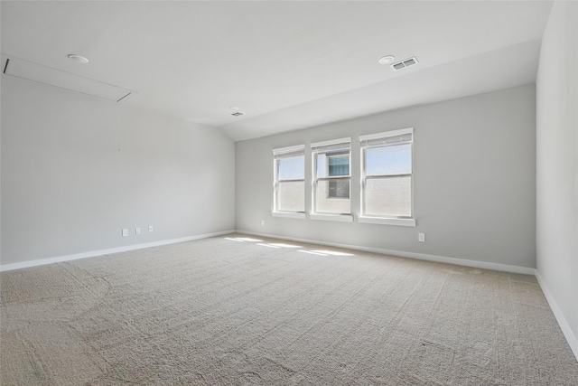 carpeted empty room with attic access, baseboards, visible vents, and vaulted ceiling