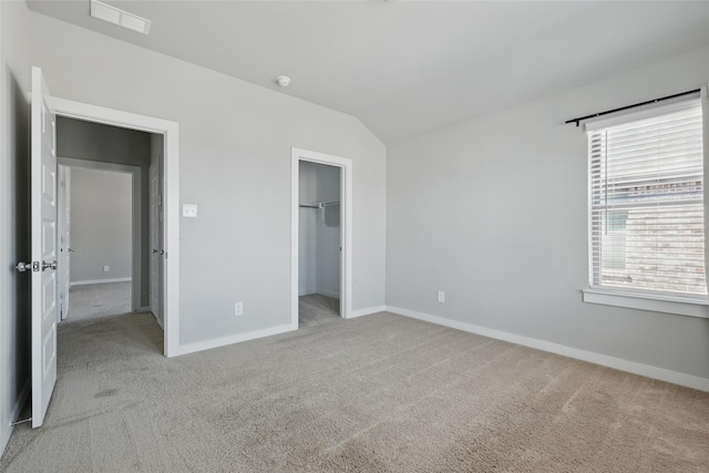 unfurnished bedroom with visible vents, baseboards, lofted ceiling, a spacious closet, and light colored carpet