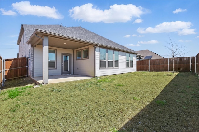 back of house featuring a lawn, roof with shingles, a fenced backyard, and a patio area