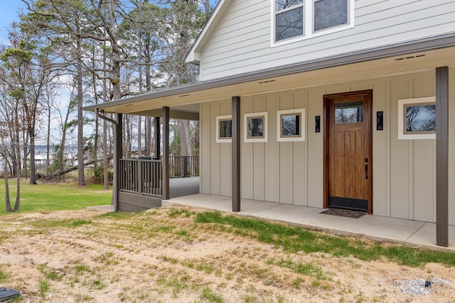 entrance to property featuring board and batten siding, covered porch, and a lawn