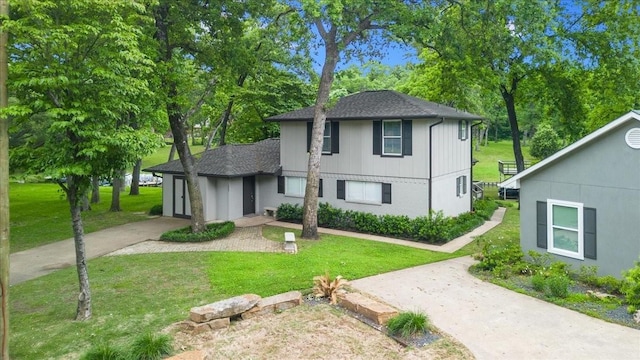 view of front of house with concrete driveway, a front lawn, and a shingled roof