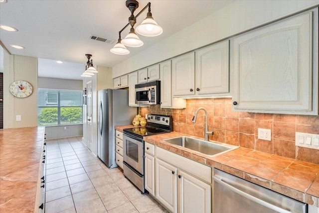 kitchen with tile countertops, light tile patterned floors, stainless steel appliances, backsplash, and a sink