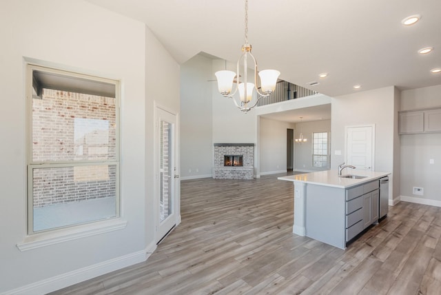 kitchen featuring a chandelier, gray cabinetry, a brick fireplace, light wood finished floors, and decorative light fixtures