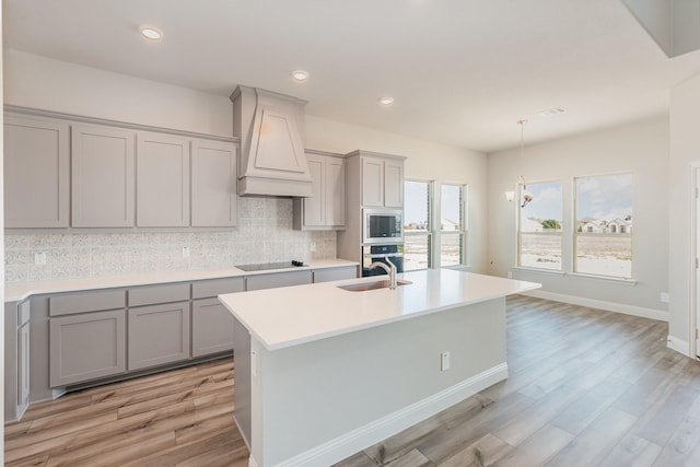 kitchen featuring stainless steel appliances, gray cabinets, light countertops, premium range hood, and backsplash