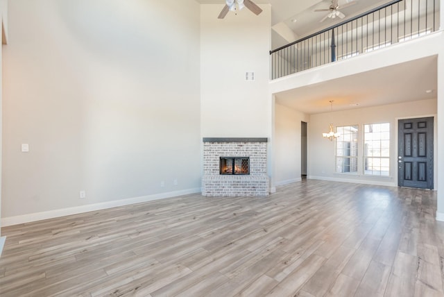 unfurnished living room featuring light wood finished floors, visible vents, baseboards, a brick fireplace, and ceiling fan with notable chandelier