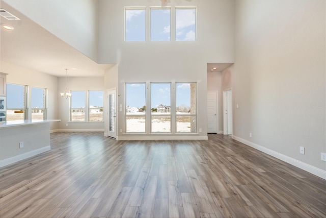 unfurnished living room featuring baseboards, wood finished floors, visible vents, and a notable chandelier