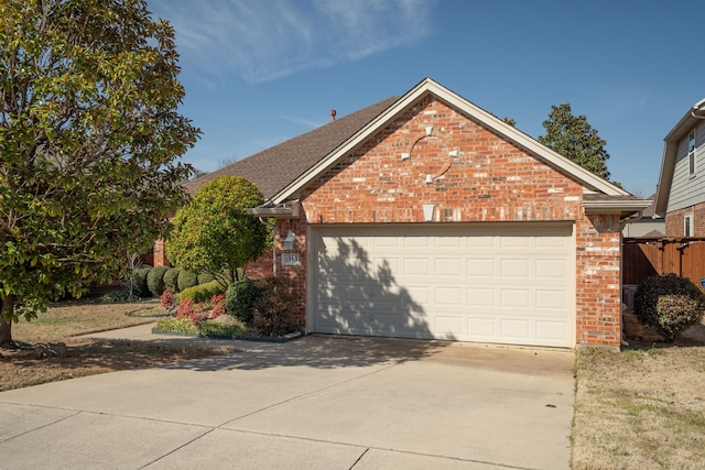 view of front facade featuring a garage, driveway, brick siding, and fence