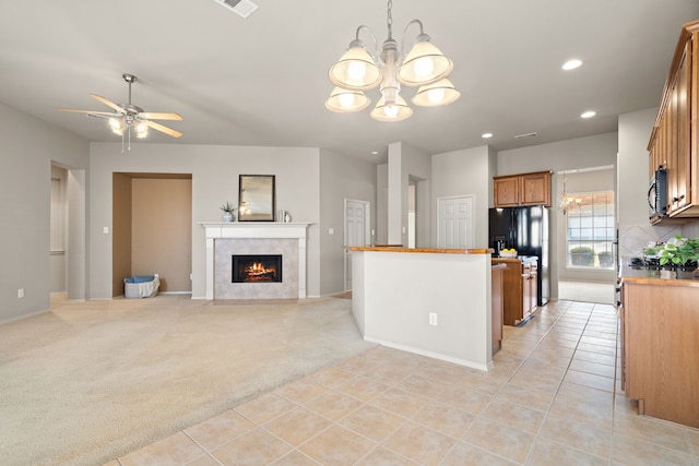 kitchen with light tile patterned floors, light colored carpet, a fireplace, black appliances, and brown cabinetry