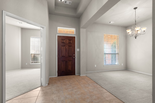 foyer featuring a notable chandelier, light tile patterned floors, visible vents, and light colored carpet