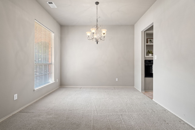 carpeted empty room with visible vents, a notable chandelier, and baseboards