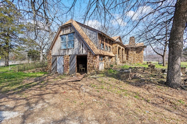 exterior space featuring a barn, stone siding, a chimney, and an outdoor structure