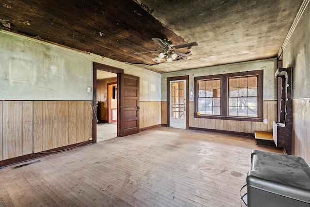 spare room featuring wooden walls, visible vents, a ceiling fan, wainscoting, and hardwood / wood-style floors