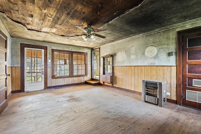 unfurnished living room with a wainscoted wall, heating unit, wood-type flooring, visible vents, and a ceiling fan