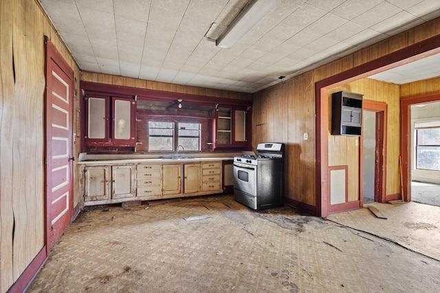 kitchen with glass insert cabinets, stainless steel range with gas stovetop, a sink, and wooden walls