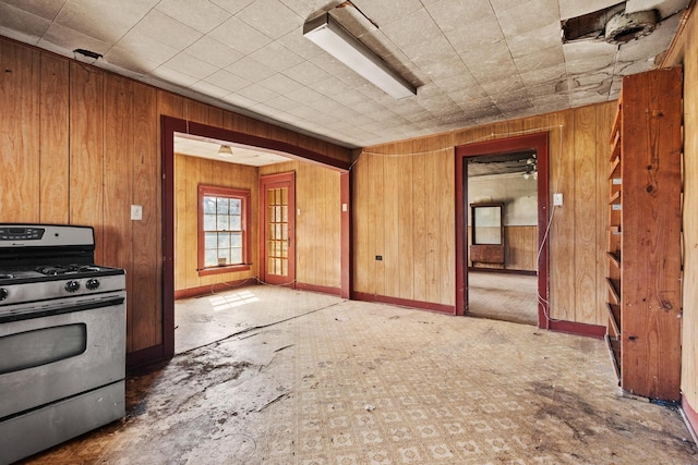 kitchen featuring wood walls, stainless steel gas range, and baseboards