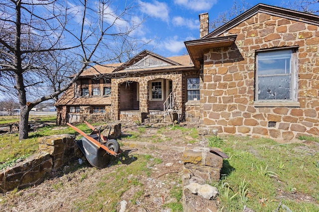 view of front of house with stone siding, a chimney, and a porch