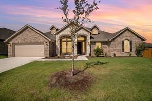 french country inspired facade with a garage, driveway, a front lawn, and stone siding